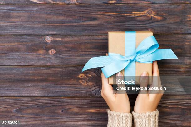 Woman Hands Give Wrapped Valentine Or Other Holiday Handmade Present In Paper With Blue Ribbon Present Box Decoration Of Gift On White Wooden Table Top View With Copy Space Stock Photo - Download Image Now