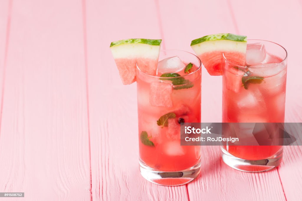 Watermelon lemonade with ice and mint leaves. Homemade lemonade of ripe berry with red and green ripes. Glass of cold watermelon tea. Refreshing summer drink. Cocktail on a wooden background Watermelon lemonade with ice and mint leaves. Homemade lemonade of ripe berry with red and green ripes. Glass of cold watermelon tea. Refreshing summer drink. Cocktail on a wooden background. Watermelon Stock Photo