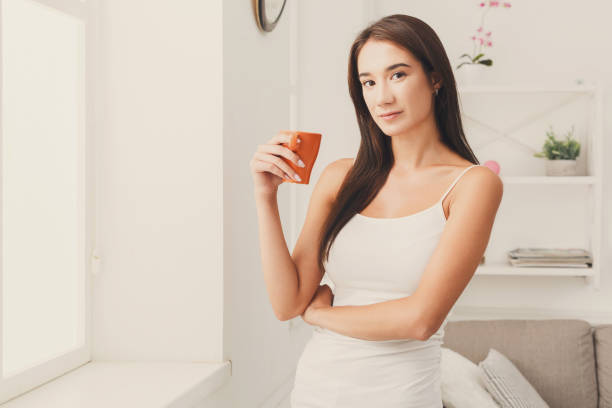 istock Serious woman standing near window with coffee 891522600