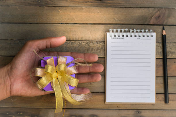 istock Holding notepad with gift and ribbon on wood board background.using wallpaper for education, business photo.Take note of the product for book with paper and concept, object or copy space. 891522886