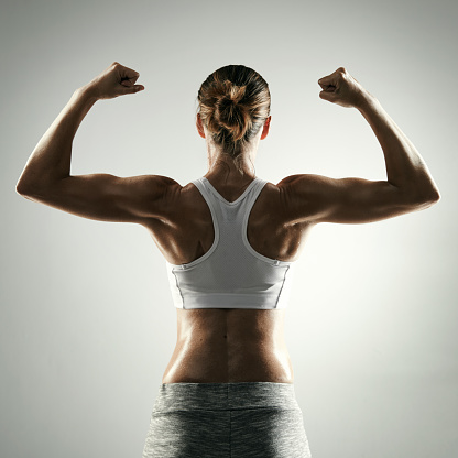 Studio shot of an unrecognizable young sportswoman flexing against a grey background