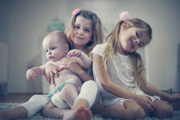 istock Two sisters poses to camera with baby brother. 891531416