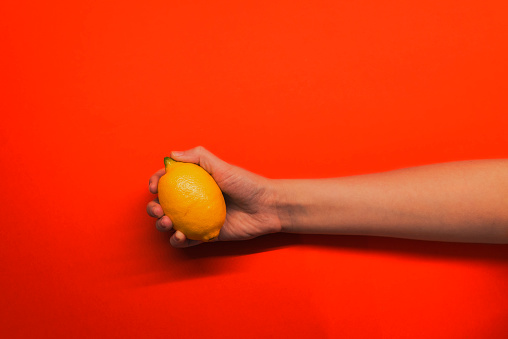 Photo of Female hand  holding fresh lemon on a red background. Home grown lemon, organic food that the girl holds in her hand. Woman holding yellow lemon citrus fruit.