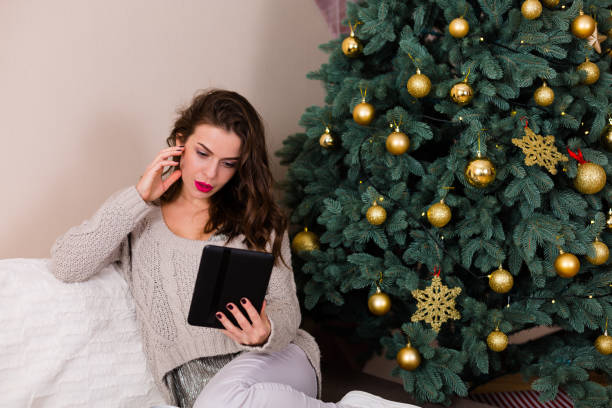 istock Woman reading e-book near the Christmas tree 891541370