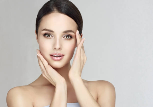 gorgeous, young woman with clean, fresh skin is touching own face.  light smile on the perfect face. cosmetology. - ayurveda massaging spa treatment wellbeing imagens e fotografias de stock