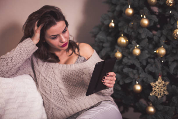 istock Woman reading e-book near the Christmas tree 891541692