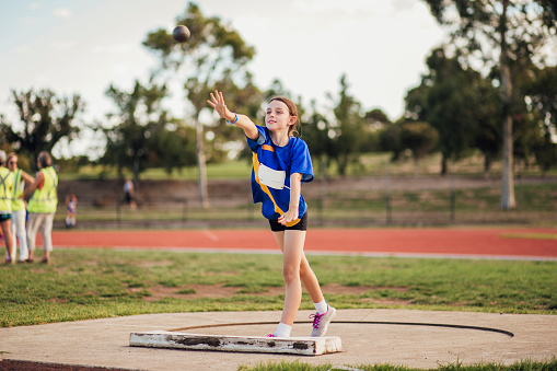 Little girl is mid-throw in a game of Shot Put at her athletics club.