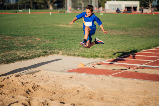 Doing A Long Jump In Athletics Club Little boy is in mid-air as he does a long jump at athletic club. track and field stadium stock pictures, royalty-free photos & images