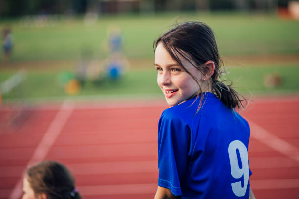 Little girl is watching over her shoulder while sitting by the running track at athletics club.