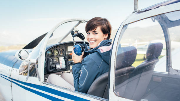 Pilot in the aircraft cockpit Smiling female pilot in the light aircraft cockpit, she is holding aviator headset and checking controls piloting photos stock pictures, royalty-free photos & images
