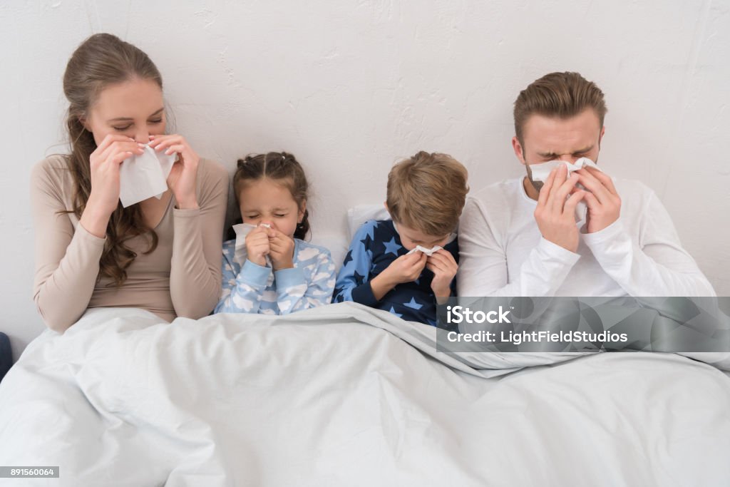 family blowing noses in napkins Sick parents ans children lying in a bed and blowing noses in napkins Family Stock Photo