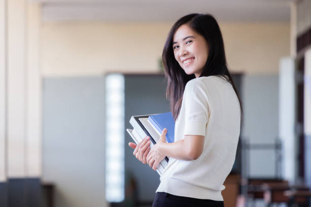 istock Asian woman holding book inside school hall way with blurry background 891573018