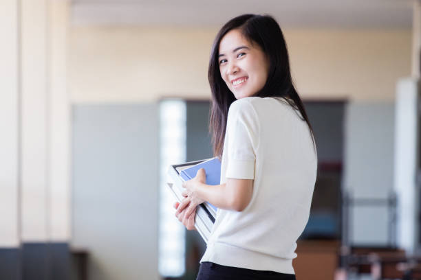 istock Asian woman holding book inside school hall way with blurry background 891576284