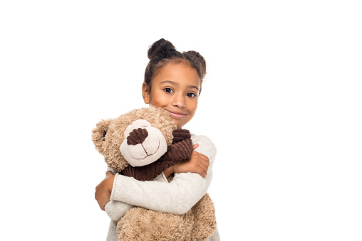 beautiful african american child hugging teddy bear and smiling at camera isolated on white
