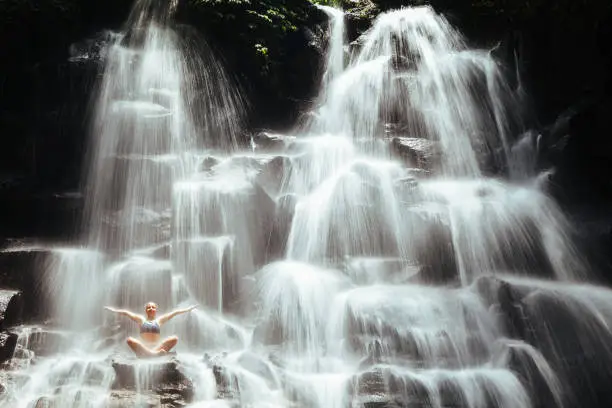 Photo of Woman sit on rock in yoga pose under cascade waterfall