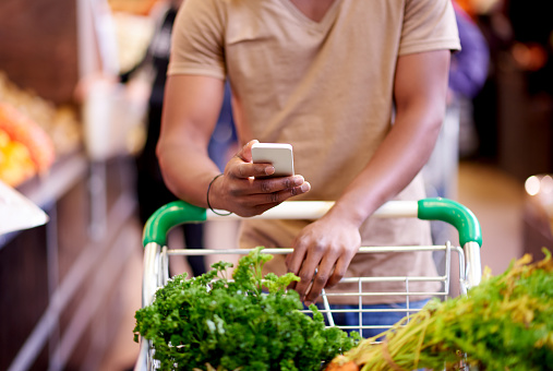 Closeup shot of an unidentifiable man using a cellphone while shopping in a grocery store