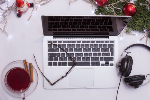 istock Top view office table desk. Workspace with laptop and christmas decorations on white background xmas lights bokeh glasses phones tea mockup 891604442
