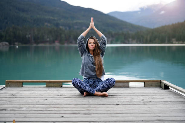 istock Young woman meditating over lake and mountain background 891605268