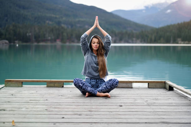 istock Young woman meditating over lake and mountain background 891605408