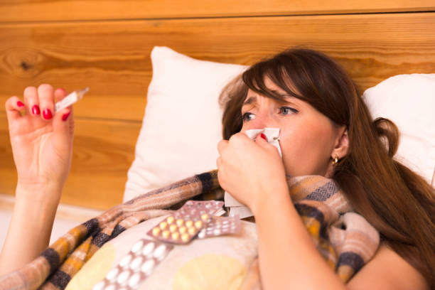 istock Sick woman in her bed looking at a clinical thermometer 891608578