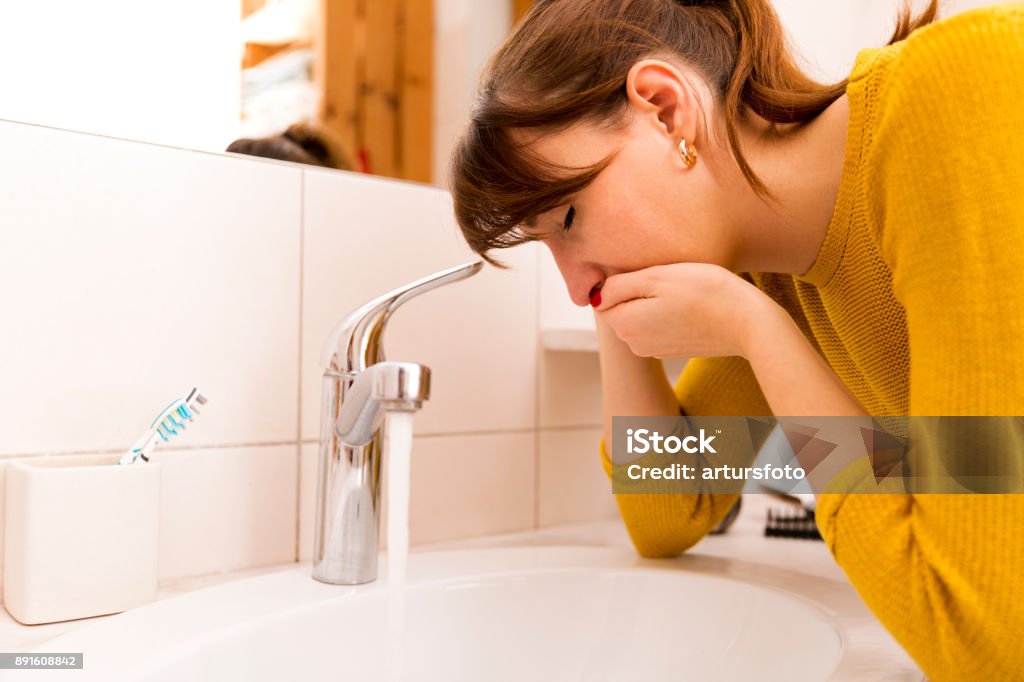 Young vomiting woman near sink in bathroom Nausea Stock Photo