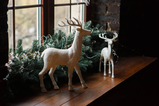 istock Christmas decoration with pine tree branches and white clay deers standing on wooden window sill 891619450