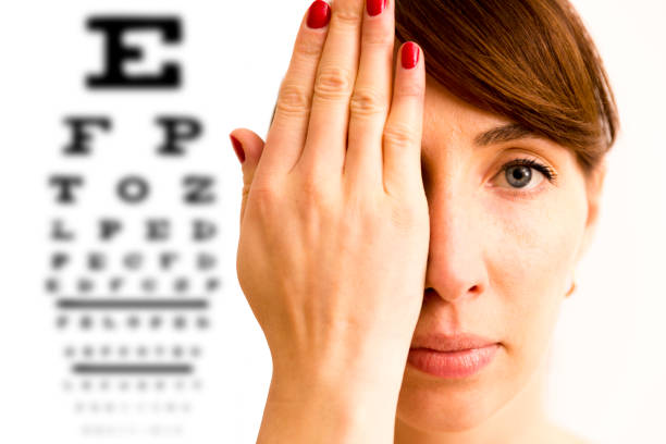 mujer joven está cubriendo su rostro con la mano y comprobar su visión. tabla de vista pruebas en segundo plano. - eye exam eyesight doctor healthcare and medicine fotografías e imágenes de stock