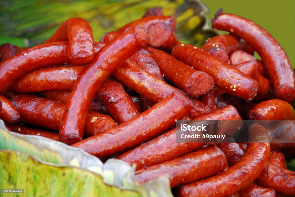 Prepaired Thai Sausage coverd with sesame seeds, A Heap of red coloured spicy Sausage laying between banana leafs. Covering Stock Photo