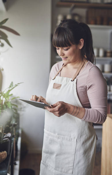 istock Smiling florist standing in her flower shop checking online orders 891634846