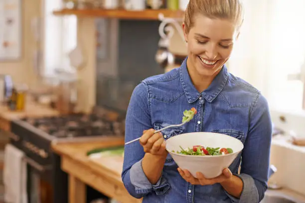 Shot of a beautiful young woman eating a healthy salad in her kitchen