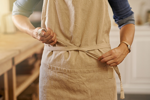 Cropped shot of a woman tying her apron in her kitchen