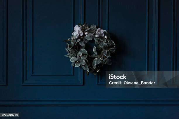 Traditional Christmas Decoration Evergreen Wreath With White Flowers Ribbon On Dark Blue Wall Background Stock Photo - Download Image Now