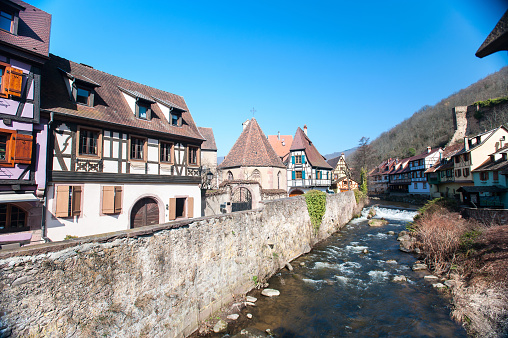 French traditional half-timbered houses and La Weiss river in Kayserberg village in Alsace, France. Outdoors horizontal summertime colored image. Blue sky cloudless background.
