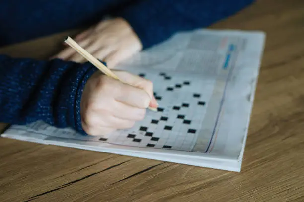 Photo of Female hand holding a pencil and solves crossword puzzle
