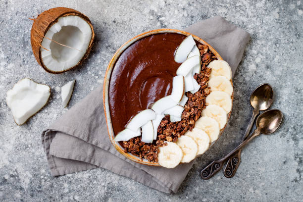 gesundes frühstück schüssel. schoko-bananen-smoothie-schüssel mit kokosflocken, müsli, bananenscheiben. ansicht von oben flach legen, overhead - powdered coconut stock-fotos und bilder