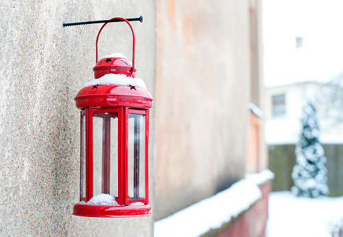 Christmas winter vintage red candle lantern hanging outside on screw on house stone wall. Garden decor. Outdoors horizontal colored image.