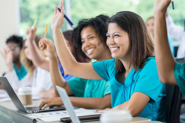 Medical students raise hands during class Diverse medical or nursing school students raise their hands to ask or answer a question during class. They are using laptop computers. asian adult student stock pictures, royalty-free photos & images