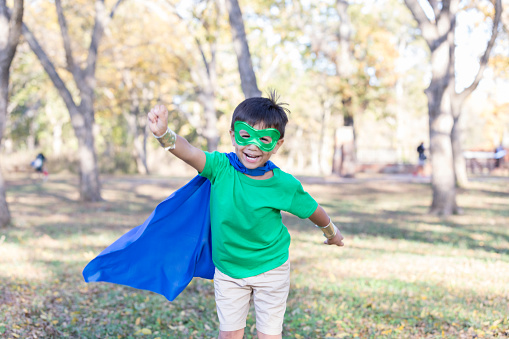 Little boy runs while pretending to be a superhero. He is wearing a homemade costume complete with mask and cape.
