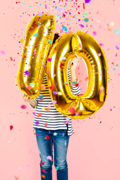 10th anniversary celebration party girl with golden balloons Little girl holding two golden balloons making the 10 number while falling confetti on a pink background. 10th anniversary celebration party. 10 11 years photos stock pictures, royalty-free photos & images