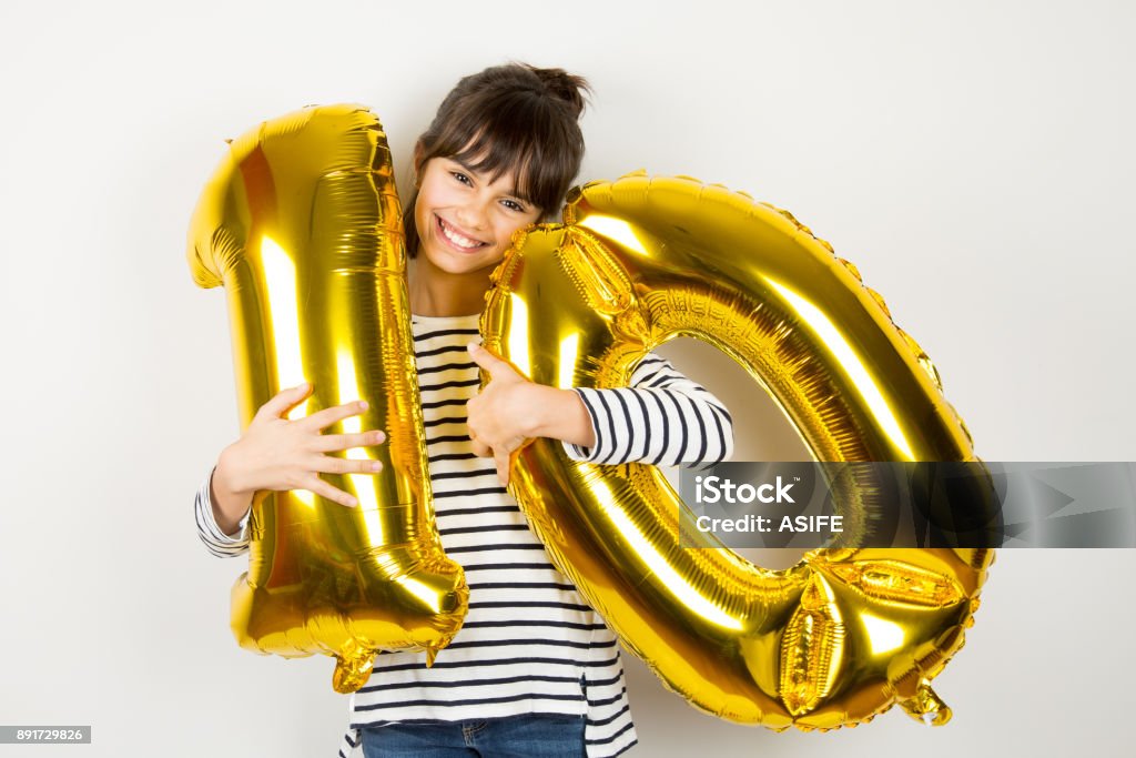 Ten birthday party girl with golden balloons Happy little girl holding two golden balloons making the 10 number on white background. 10th anniversary celebration party. 10-11 Years Stock Photo