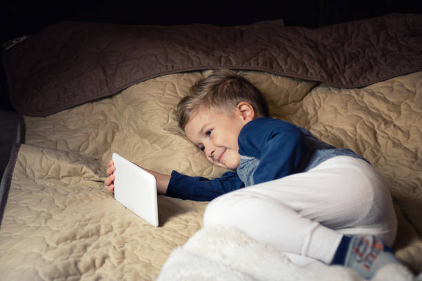 istock Happy kid watching cartoons on touchpad while resting on the bed. 891769200