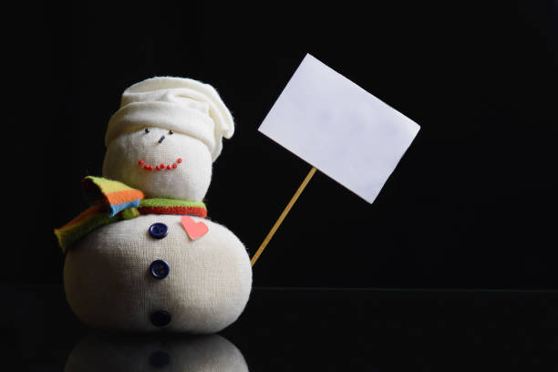 Snowman holding placard board with stick attached. Low key photograph.