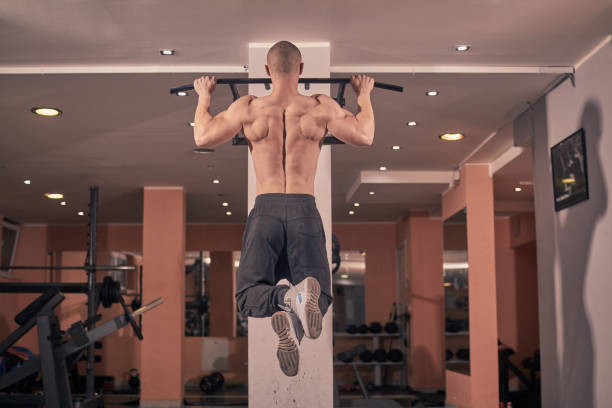 un giovane bodybuilder, vista posteriore, palestra pull-up bar, palestra al chiuso. riprese a figura intera. - lenght foto e immagini stock