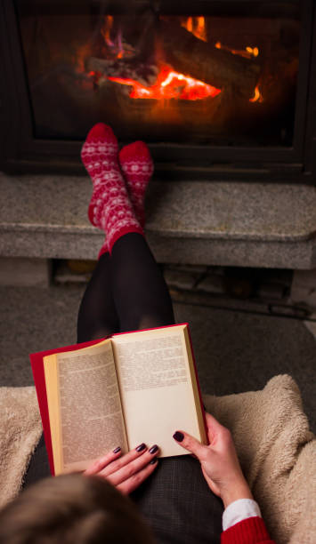 istock Female reading a book by the fireplace 891806614