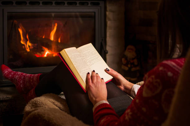 istock Female reading a book by the fireplace 891806818