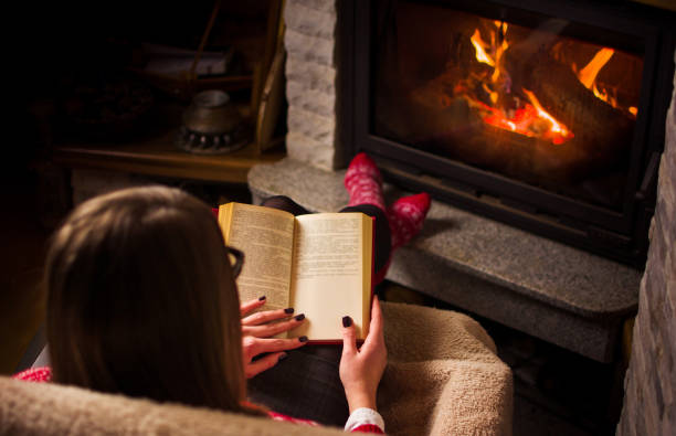 istock Female reading a book by the fireplace 891806894