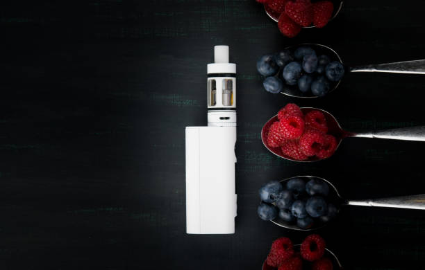 istock white electronic cigarette on a black background, with different flavors of berries on it 891807128