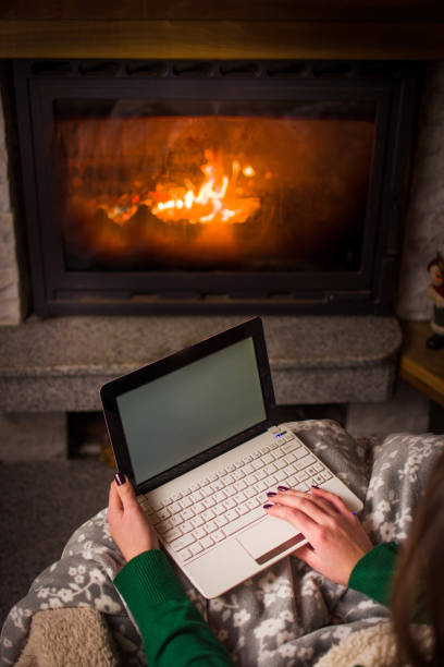 istock Woman using laptop by the fireplace at home 891807274