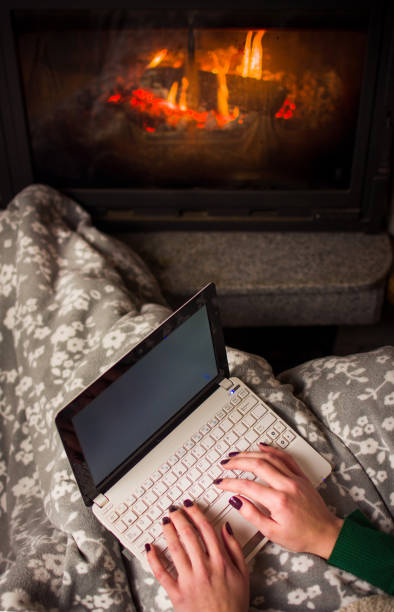 istock Woman using laptop by the fireplace at home 891809824