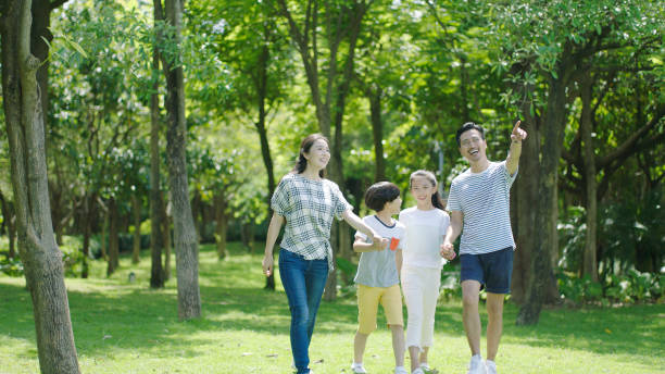 Asian parents & kids walking outdoors on summer weekend & laughing stock photo